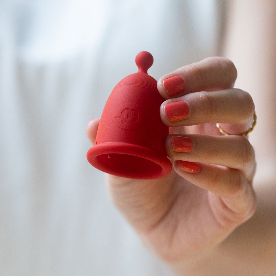 A hand holding a red menstrual cup.