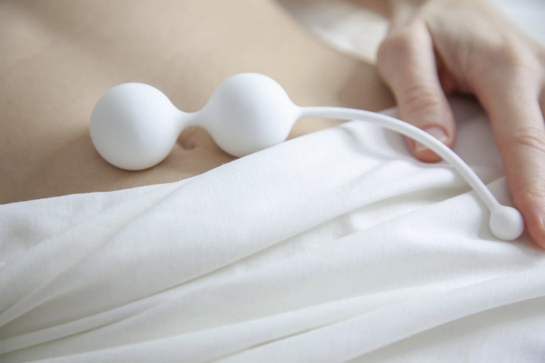 A close-up view of a woman lying down with white Whoop·de·doo Kegel balls resting on her lower abdomen.
