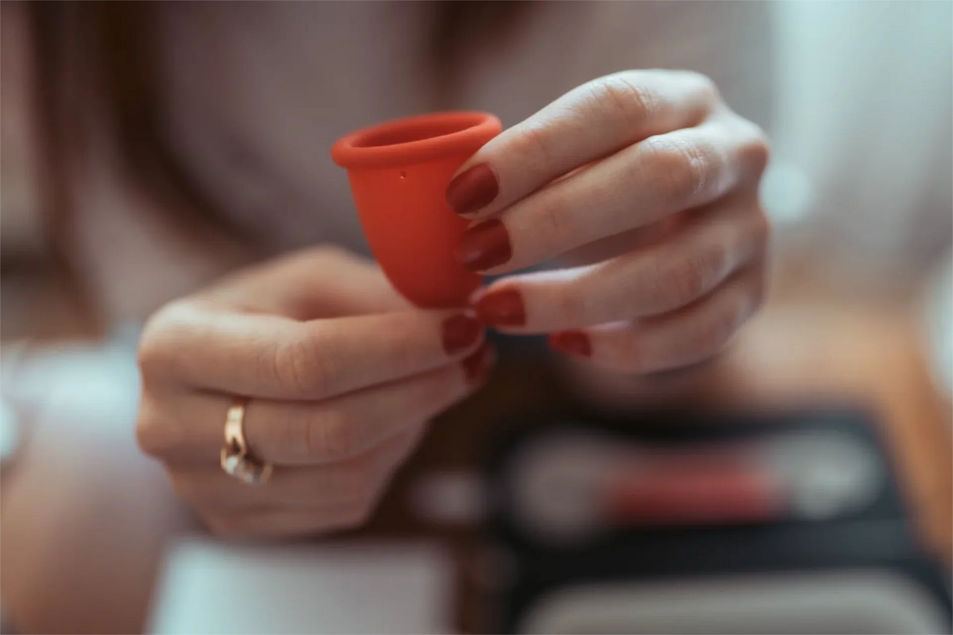 Woman's hands squeezing a red Whoop·de·doo medical silicone menstrual cup.