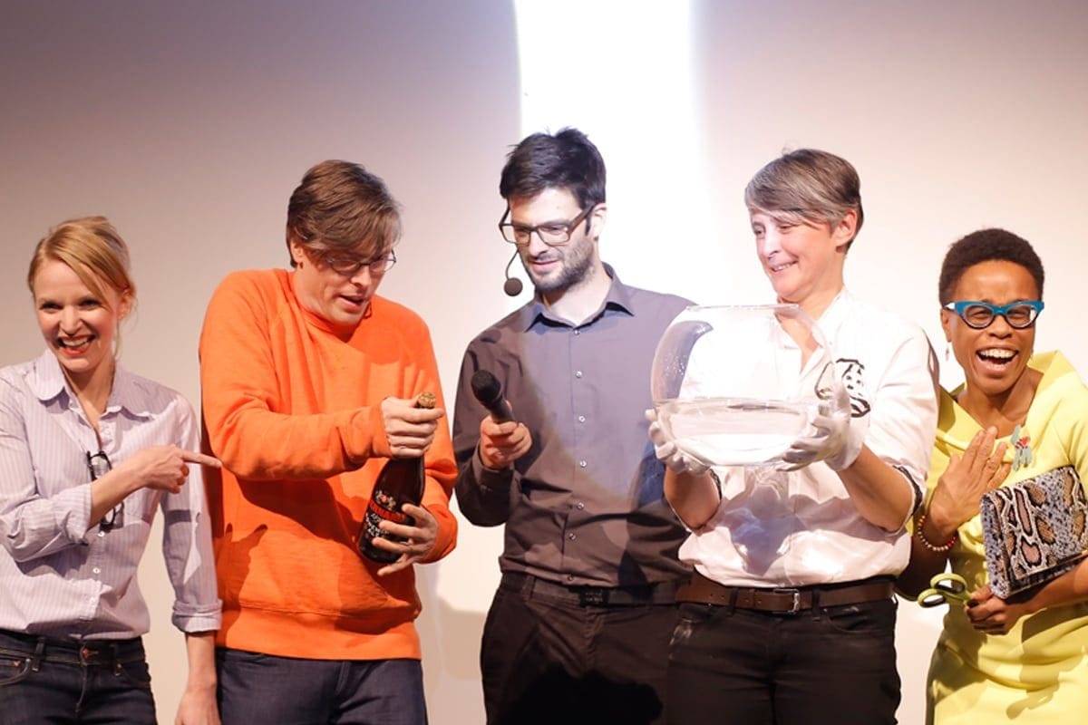 Slavnostní křest vibrátoru Whoop·de·doo v Hauch Gallery. Na pódiu stojí pět usmívajících se lidí, včetně Anny Marešové a kmotrů produktu, kteří drží skleněnou mísu a láhev šampaňského.