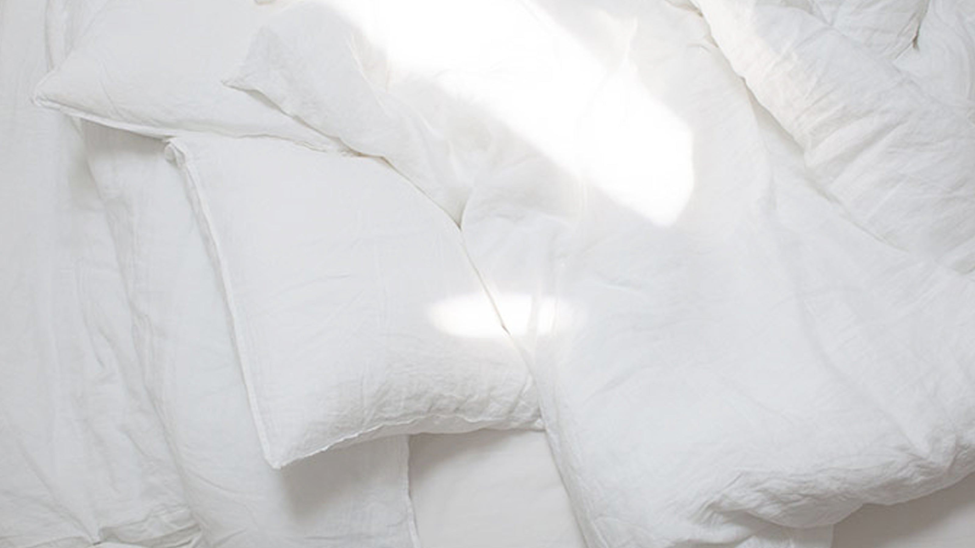 Sunlit unmade bed with white linen capturing morning intimacy and cozy bedroom lifestyle.