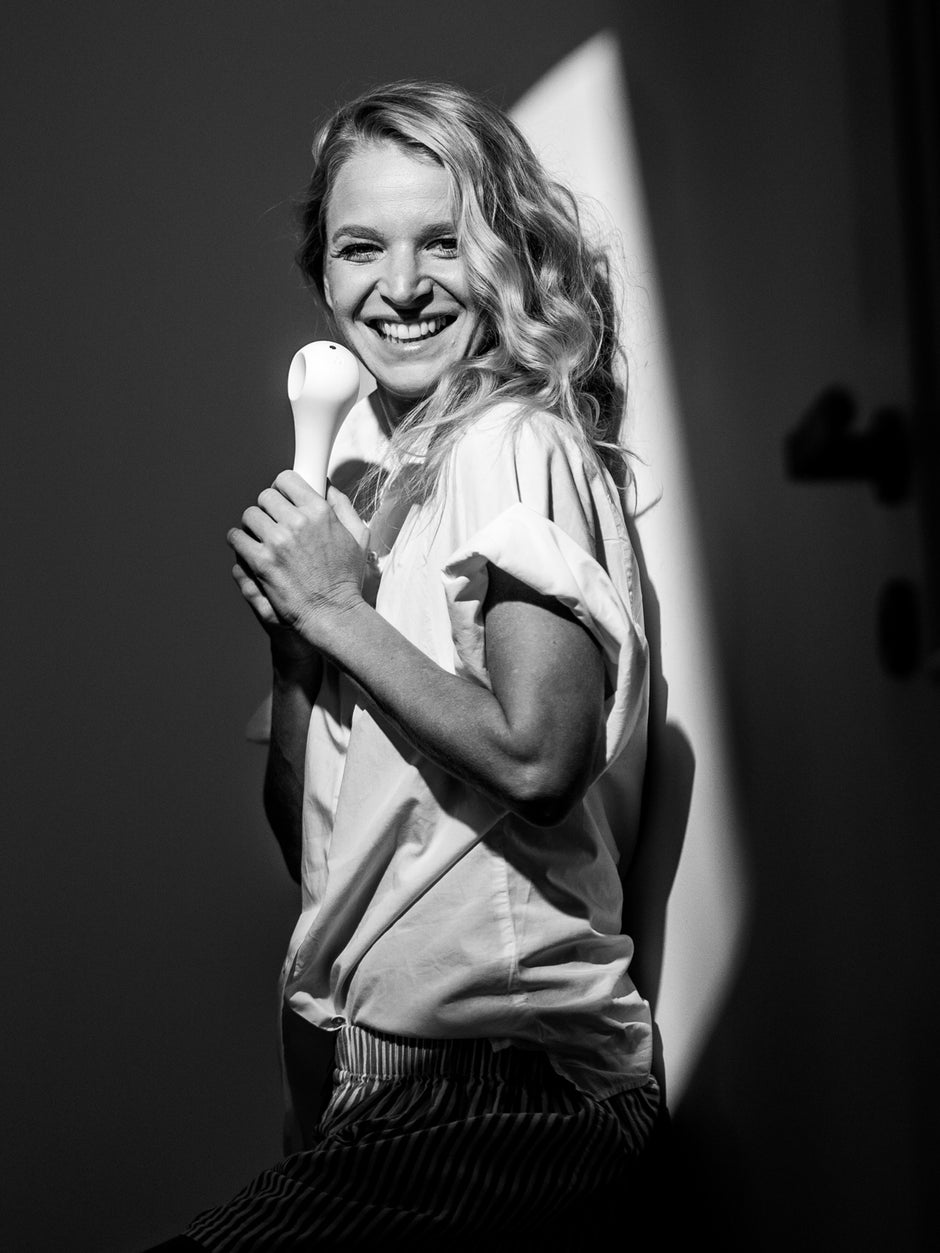 Black and white photo of smiling designer Anna Marešová holding a white Whoop-de-doo Classic vibrator.