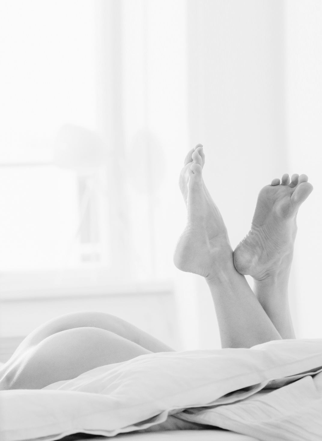 Black and white artistic shot of a woman's legs in bed, embodying intimate wellness and the quiet perfection of Whoop-de-doo care.  