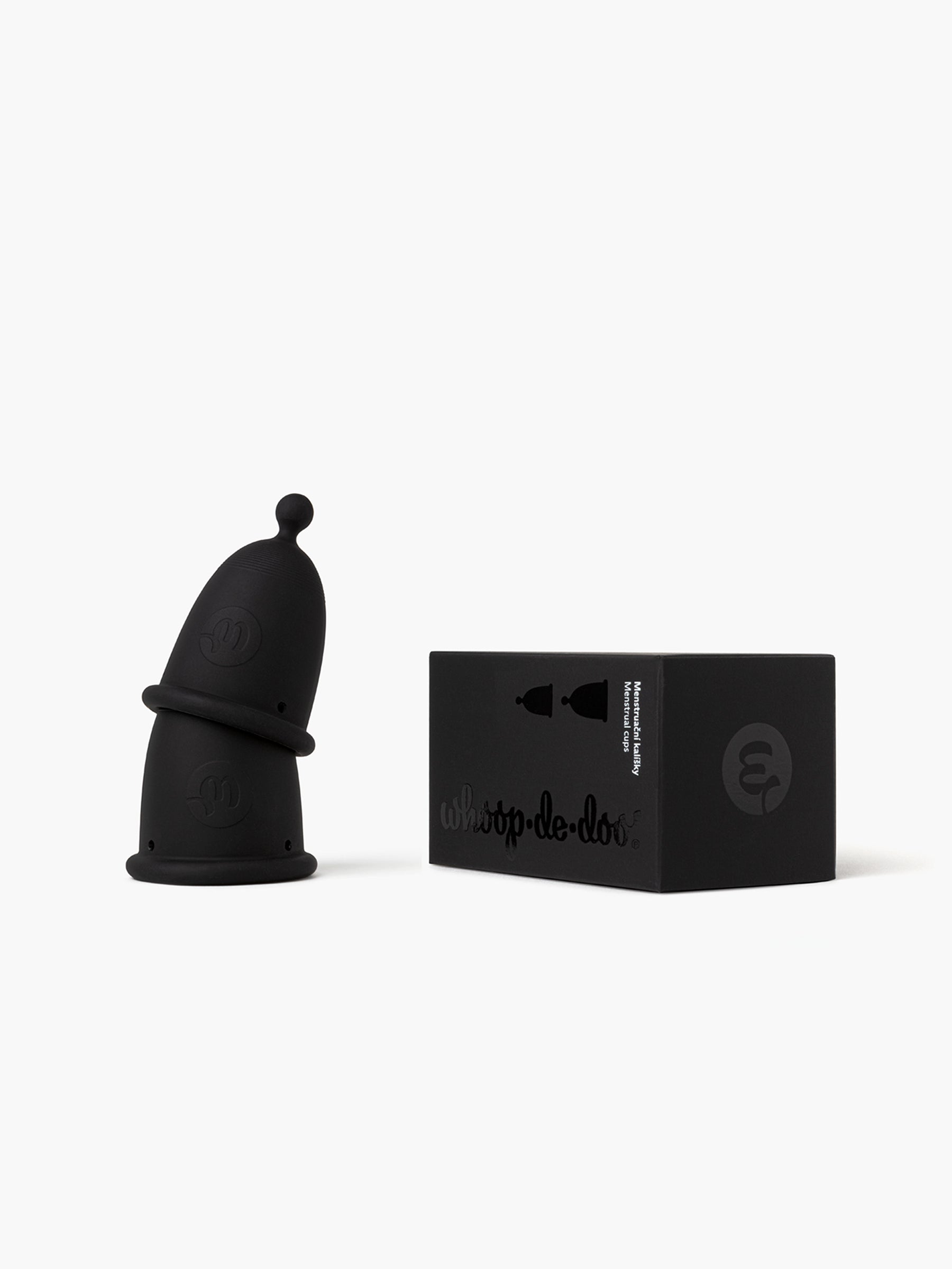 Two black-grey Whoop-de-doo menstrual cups from the Duo pack stacked on top of each other next to their elegant black packaging box on a white background.