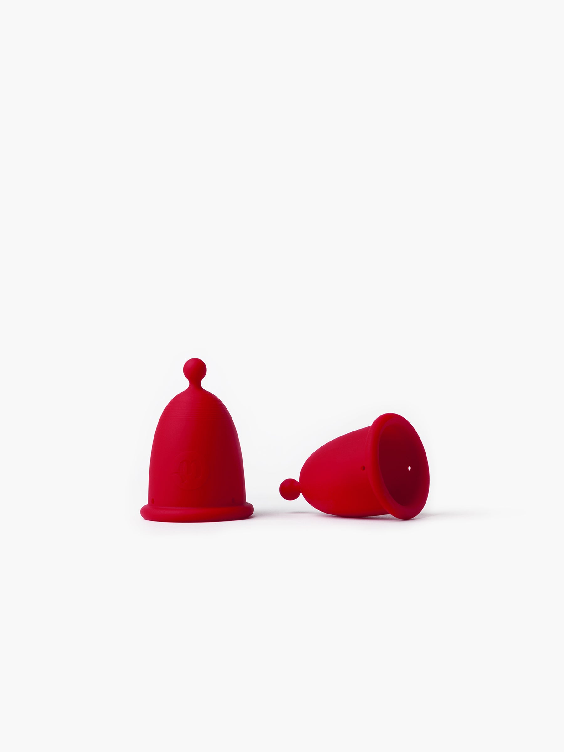 Red Whoop-de-doo menstrual cups from the Duo pack displayed side by side – one standing and one lying down to showcase the inner space and design details.