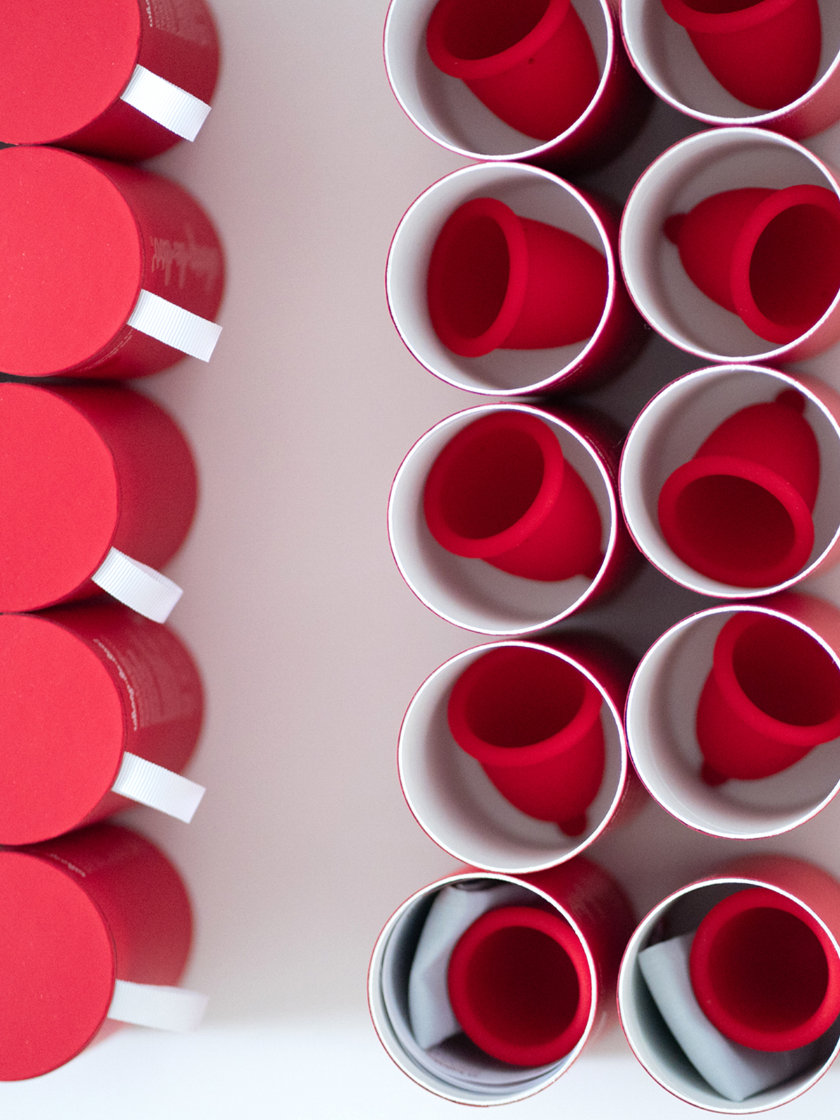 Top-down view of vibrant red Whoop-de-doo menstrual cups inside cylindrical tubes during the packaging process.