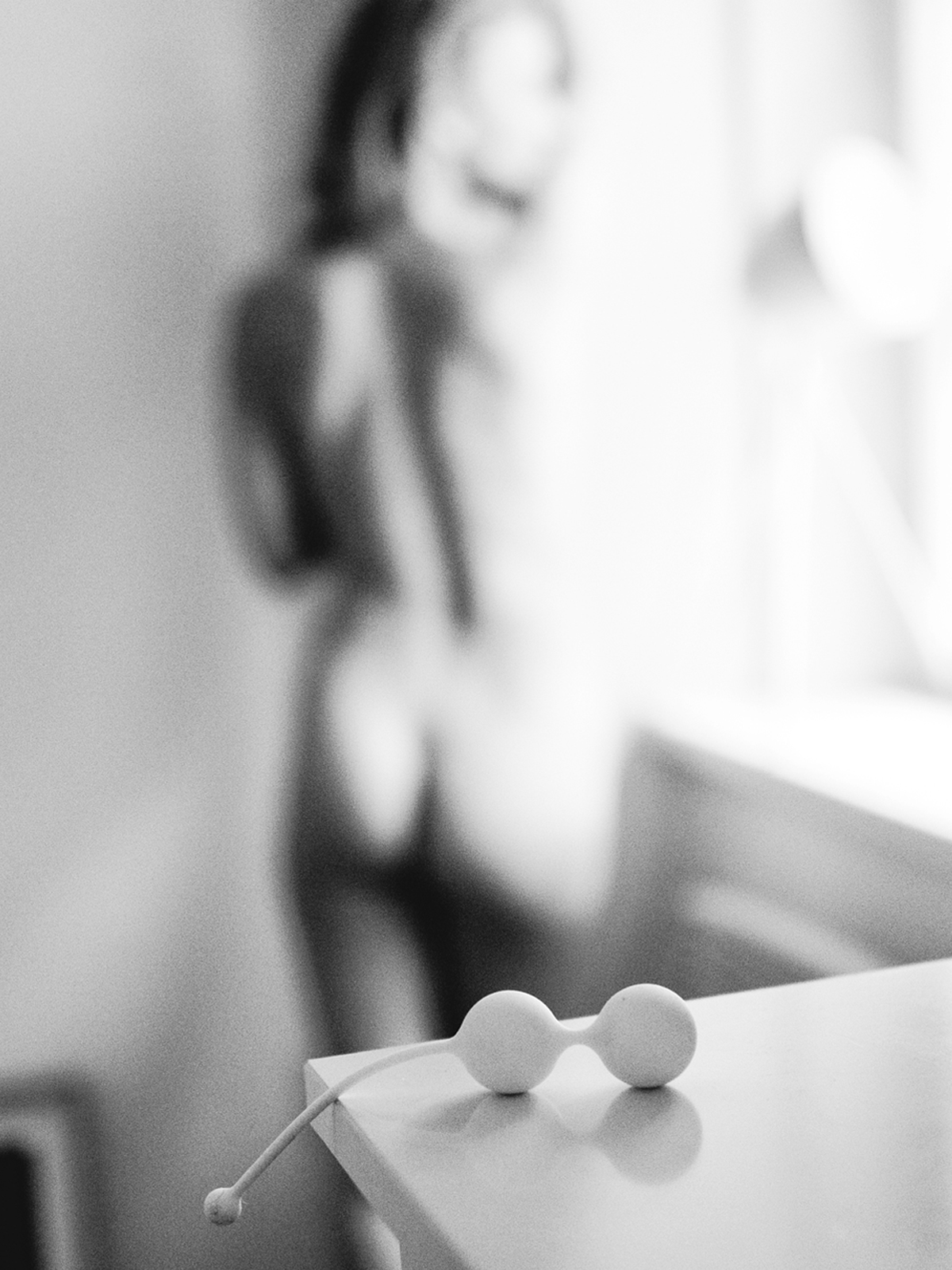 White Whoop-de-doo Light pelvic floor weights on a desk with a blurred female silhouette in the background.